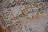 Distressed vintage Oushak runner texture: worn beige, brown, and soft pink floral motifs.