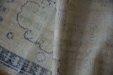 Distressed vintage Oushak rug showing worn pile, visible foundation, and faded blue motifs.