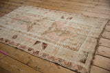 Distressed vintage Melas rug corner, blush pink, ivory tones, geometric border, and fringe.