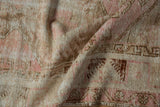 Distressed texture detail of Melas rug, with pink, ivory, and chocolate brown geometric motifs.