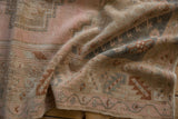 Folded vintage distressed Melas rug showing worn pile, blush, rose, and slate blue geometric patterns.