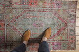 Distressed vintage Oushak rug pile with faded red, pink, and sage green motifs.