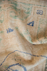 Distressed Oushak rug pile with visible foundation, ivory, pale green, and cobalt blue motifs.