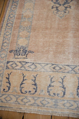 Distressed Oushak rug corner displaying beige field, cobalt blue patterns, and visible foundation wear.