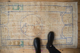 Distressed Oushak rug, muted ivory field showing low pile, faded cobalt blue curvilinear patterns.