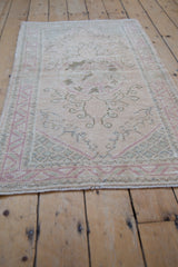 Distressed Oushak rug pile revealing faded scrolling vinery in soft ivory and rose.