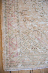 Distressed vintage Oushak rug edge showing pile wear, intact selvage, faded rose and seafoam.