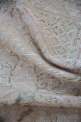 Distressed Oushak rug texture, showing wear to foundation with pale rose and seafoam tones.
