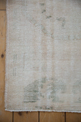 Distressed vintage Oushak runner corner, revealing worn ivory and faded green pile, with intact selvage.