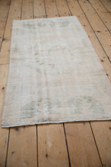 Corner detail of a distressed vintage Oushak runner, highlighting worn ivory pile and soft green pattern.