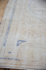 Distressed Oushak rug showing worn ivory pile, exposed foundation, and faint blue motifs.