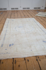Angled view of distressed Oushak rug, faded ivory and cobalt blue floral medallion.
