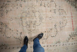Distressed vintage Oushak carpet showing worn ivory, blush, seafoam green pile with charcoal scrolling vinery.