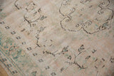 Distressed Oushak rug pile close-up: ivory, blush, seafoam green, scrolling vinery, mostly even wear.