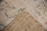 Distressed ivory and blush pile of vintage Oushak rug with visible woven foundation.