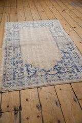 Angled view of a distressed vintage Oushak rug with faded denim blue prayer motifs on antique ivory, showing wear to knot heads.