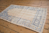 Distressed Oushak rug corner: faded blue pattern on antique ivory, foundation visible.