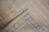 Folded vintage distressed Oushak rug, showing worn pile with foundation visible and blue patterns.