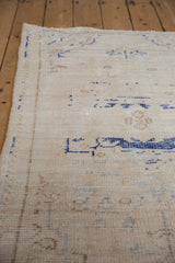 Distressed Oushak rug shows intact side selvage, worn pile, faded cobalt patterns.