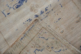 Distressed ivory Oushak rug corner showing pile wear, cobalt motifs, exposed foundation, and selvage.