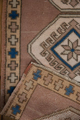 Distressed Oushak rug folded edge, revealing beige mauve and blue hook and latch motif.