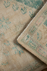 Folded vintage Oushak rug showing distressed pile, exposed foundation, and intact side cording.