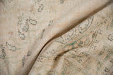 Distressed Oushak carpet pile showing worn ivory, blush, and deep green vinery.