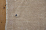Beige vintage Oushak rug's worn pile, original selvage, and small navy shrub motif.