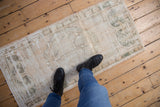 Distressed Oushak rug runner with visible knot heads and faded ivory, green motifs.