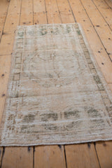 Distressed vintage Oushak runner with worn pile, ivory, beige, and soft green Rococo patterns.