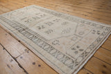 Distressed ivory Oushak rug showing faded oxidized silver patterns and visible pile wear.