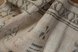 Distressed texture and geometric patterns in ivory and beige on a vintage Oushak rug.