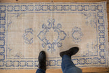Distressed vintage Oushak rug featuring cobalt blue starburst border on an ivory field.