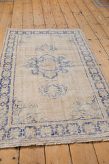 Distressed vintage Oushak rug with faded cobalt blue starburst border and aged ivory field.