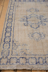 Distressed vintage Oushak rug close-up: faded cobalt blue geometric border, beige field.