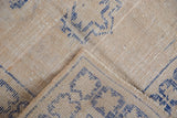 Distressed Oushak rug pile showing cobalt blue geometric motifs, selvage, and foundation wear.