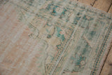 Distressed vintage Oushak carpet showing worn pile, pale beige pink, and ocean turquoise border.