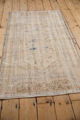 Distressed Oushak rug with worn ivory pile and subtle faded blue geometric patterns.