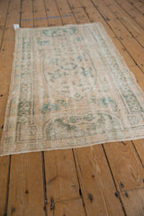 Distressed Oushak rug showing faded ivory and seafoam green floral medallion with textured wear.