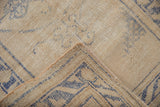 Distressed Oushak rug's soft ivory pile, faded denim blue pattern, and side cording.