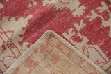 Distressed Oushak rug corner displaying worn dusty raspberry pile, beige foundation, and selvage.