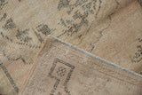 Distressed Oushak rug corner, showing mostly even wear, visible foundation, and side selvage.