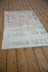 Textured distressed vintage Oushak rug: worn ivory field, blue motifs, visible foundation.