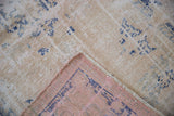 Vintage Distressed Oushak rug corner revealing worn ivory pile, faded blue motifs, and pink reverse.