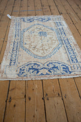 Fringed bottom corner of a distressed Oushak rug, showing deep denim blue border and worn ivory field.