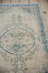 Distressed beige Oushak rug pile with denim blue roundel outline and seafoam green scrolls.
