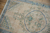 Distressed Oushak rug with ivory field, seafoam green scrolling, and denim blue geometric border.