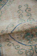 Distressed vintage Oushak rug close-up, worn texture with ivory, blue, and green scrolling motifs.