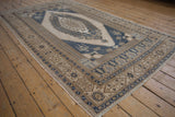 Distressed vintage Oushak carpet corner with beige and denim blue geometric and stylized border.