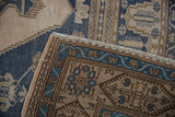 Distressed Oushak rug corner showing teal geometric border, fringe, and dusty blue field.